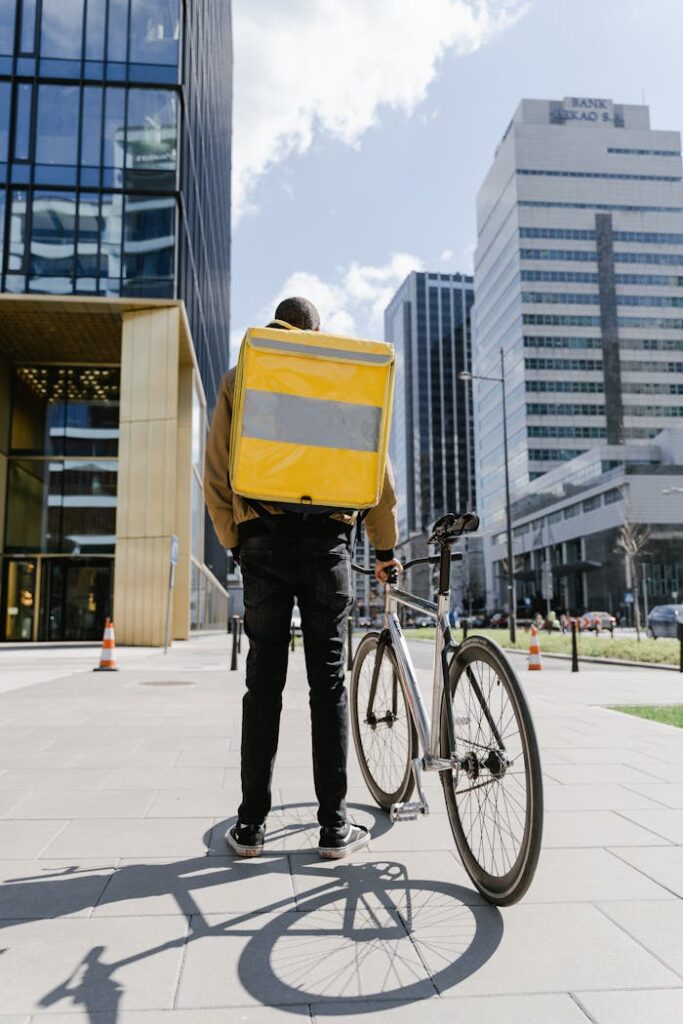 A courier stands with a bicycle and yellow delivery bag in downtown Warsaw, showcasing urban delivery dynamics.